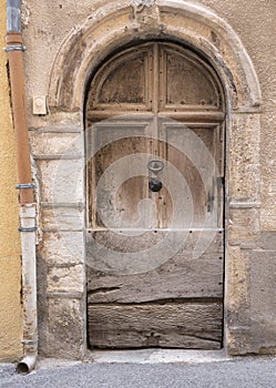 Very old weathered brown door in ancient wall of medieval village in french provence