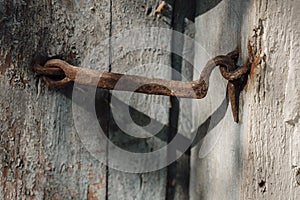 Very rusty door hook closing a wooden door, closeup. An old wooden gate locked with an equally old rusty hook . Vintage background