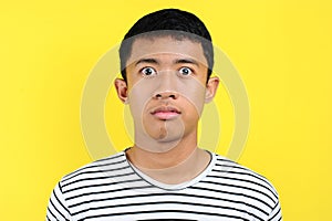 Very serious young Asian man looking at camera  on yellow