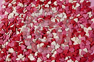 Very small heart-shaped candies are scattered across the background. Many small bright hearts in bulk