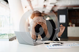 Very stressed business asian woman sitting in front of her computer looking at a large pile of paperwork, while holding