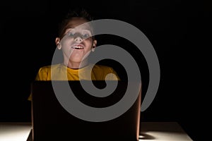 Very surprised boy sitting in the dark in front of a laptop screen, his eyes wide and mouth open