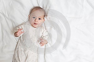 Very surprised and impressed  little baby girl lying on a white bed. Copy space at the right