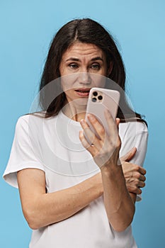 a very surprised woman stands on a blue background in a white T-shirt with a fashionable phone in her hands and looks at