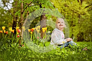 Very sweet beautiful blonde girl sits near the flower bed of red