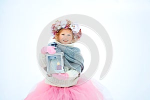 Very sweet beautiful little smiling girl child in pink skirt and mittens, white pullover, gray scarf and floral wreath with old