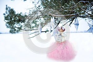 Very sweet beautiful little smiling girl child in pink skirt, white pullover, gray scarf and floral wreath with lantern in hands.