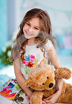 Very sweet smiling curly haired young girl sitting on the bed wi