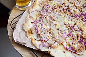 Very tasty and delicious pizza with tuna, red onion, cheese. Thin Italian pastry. Close-up, top view. A glass of cold light beer