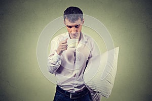 Very tired, falling asleep business man holding a cup of coffee and pillow