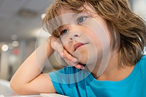 Very unhappy sad kid looks away. Boy waiting for someone in the cafe.