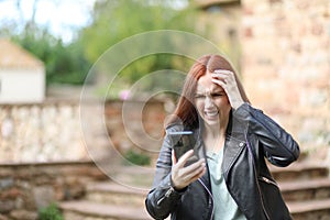 Very upset woman with her hand on her forehead contemplates what she sees on her mobile phone