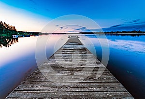 Very very long wooden bridge, almost to horizon, on the calm lake, summer sunset - blue rose skies reflected in still water.