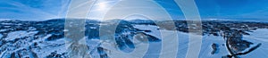 Very wide scenic aerial panorama on frozen lake, mountains with snow mobile traces, sunny blue sky with plane traces, contrails.