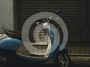 A Vespa styled scooter is parked in a dark street of Tokyo by night