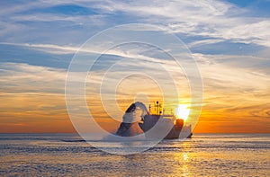 Vessel engaged in dredging at sunset time. Hopper dredger working at sea. Ship excavating material from a water