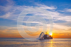 Vessel engaged in dredging at sunset time. Hopper dredger working at sea. Ship excavating material from a water