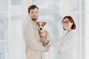 Vet female and male pet owner poses with favourite dog, come to veterinary office or hospital for doctor checkup, stand together photo