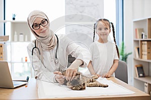 Vet with syringe and tween girl posing near cat on table