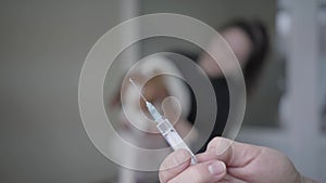 Veterinarian picks up the medicine in the syringe on the foreground. The blurred figure of woman petting her big dog