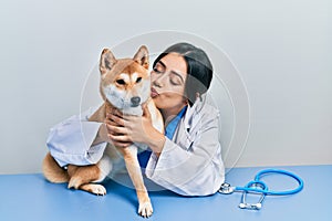 Veterinarian woman wearing uniform at the clinic, hugging dog with love