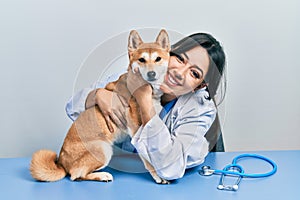 Veterinarian woman wearing uniform at the clinic, hugging dog with love