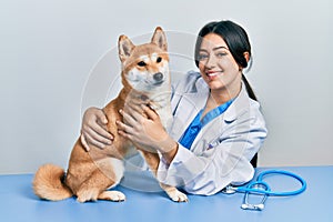 Veterinarian woman wearing uniform at the clinic, hugging dog with love