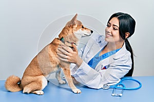 Veterinarian woman wearing uniform at the clinic, hugging dog with love