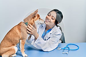 Veterinarian woman wearing uniform at the clinic, hugging dog with love