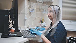 The veterinarian at work is typing on the keyboard at the computer.