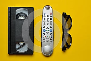 Vhs, TV remote, 3d glasses on a yellow paper background. Entertainment 90s. Top view.