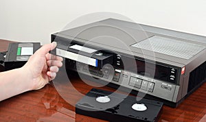 VHS videocassette is put into the video recorder to watch the video, another video cassette is on the video-tape recorder