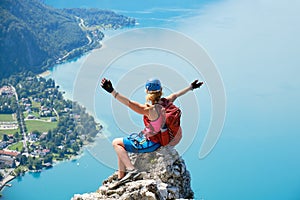Via ferrata woman climber sits on top of a rock at Attersee, Austria, and spreads her arms. Happiness, courage, adventure, active