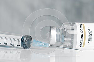 Vial of coronavirus Covid-19 vaccine and an hypodermic syringe on a white reflective surface