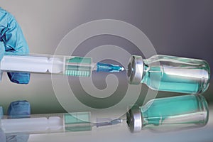 Vial filled with liquid vaccine in medical lab with syringe.doctor`s hand holds ampoule and syringe on glass surface