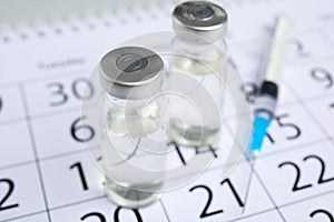 Vial and syringe on calendar. Vaccination and immunization