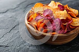 A vibrant assortment of baked vegetable chips served in a rustic wooden bowl on a dark slate background