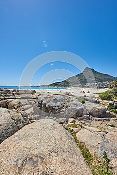 Vibrant beach near rocky shore and mountains on blue sky background with copy space. Bright summer with tourists tanning