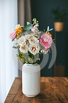 A vibrant bouquet of flowers in various colors and types, arranged in a white vase on a wooden table