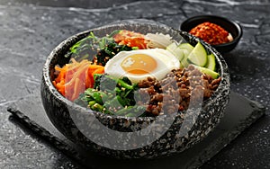 A vibrant bowl of Bibimbap, a Korean mixed rice dish, topped with colorful vegetables, beef, and a fried egg.