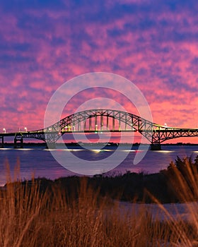 Vibrant colorful sunset sky behind a long steel tied arch bridge. Fire Island New York