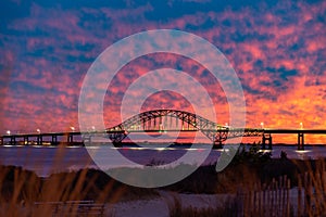 Vibrant colorful sunset sky behind a long steel tied arch bridge. Fire Island New York