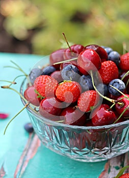 Vibrant colors of summer berries on a garden table. Blurry green background with copy pace.