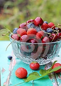 Vibrant colors of summer berries on a garden table. Blurry green background with copy pace.