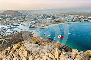 Vibrant flag waving in the foreground of a picturesque cityscape. Cabo San Lucas, Mexico.