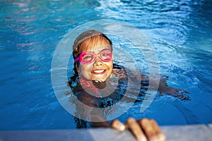 Vibrant joy in the pool: a child with pink goggles smiles in the water.