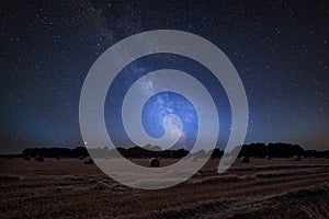 Vibrant Milky Way composite image over landscape of field of hay bales in countryside