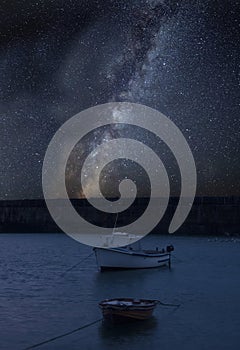 Vibrant Milky Way composite image over landscape of Fishing boats in harbour