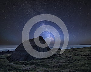 Vibrant Milky Way composite image over landscape of seaweed drying hut at Freshwater West beach in Wales