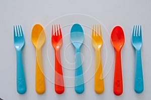 Vibrant multicolored forks, kives and spoons white background